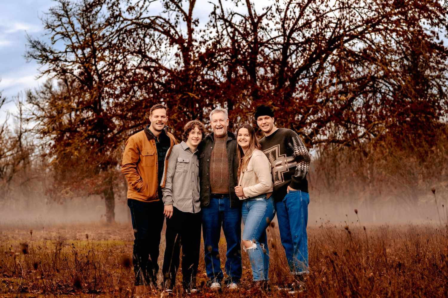 Group portrait of family members standing together in autumn field.