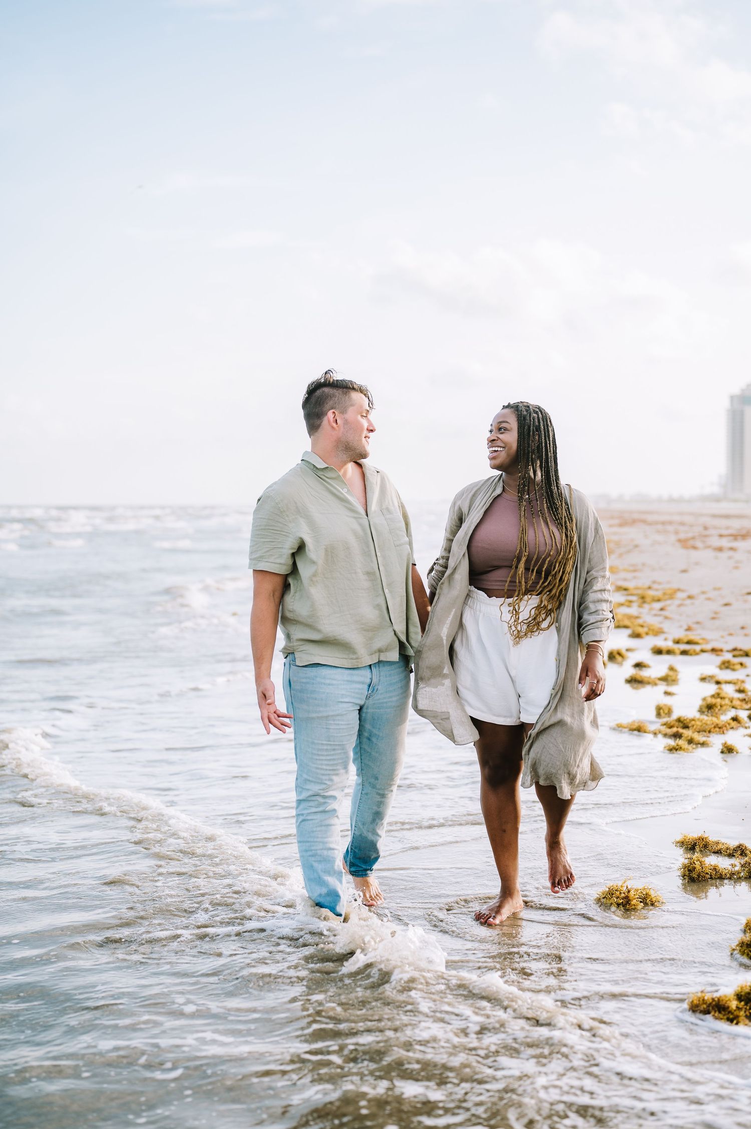 Couple enjoying playful moment in ocean waves during sunset beach photoshoot.