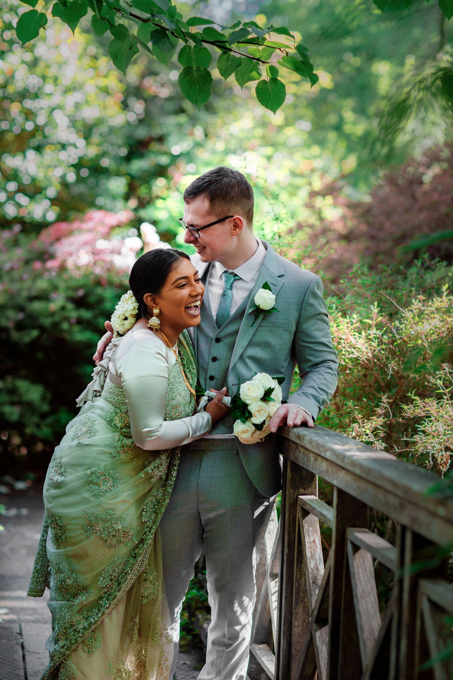 Joyful wedding portraits of a couple in grey and green attire on a rustic wooden bridge.