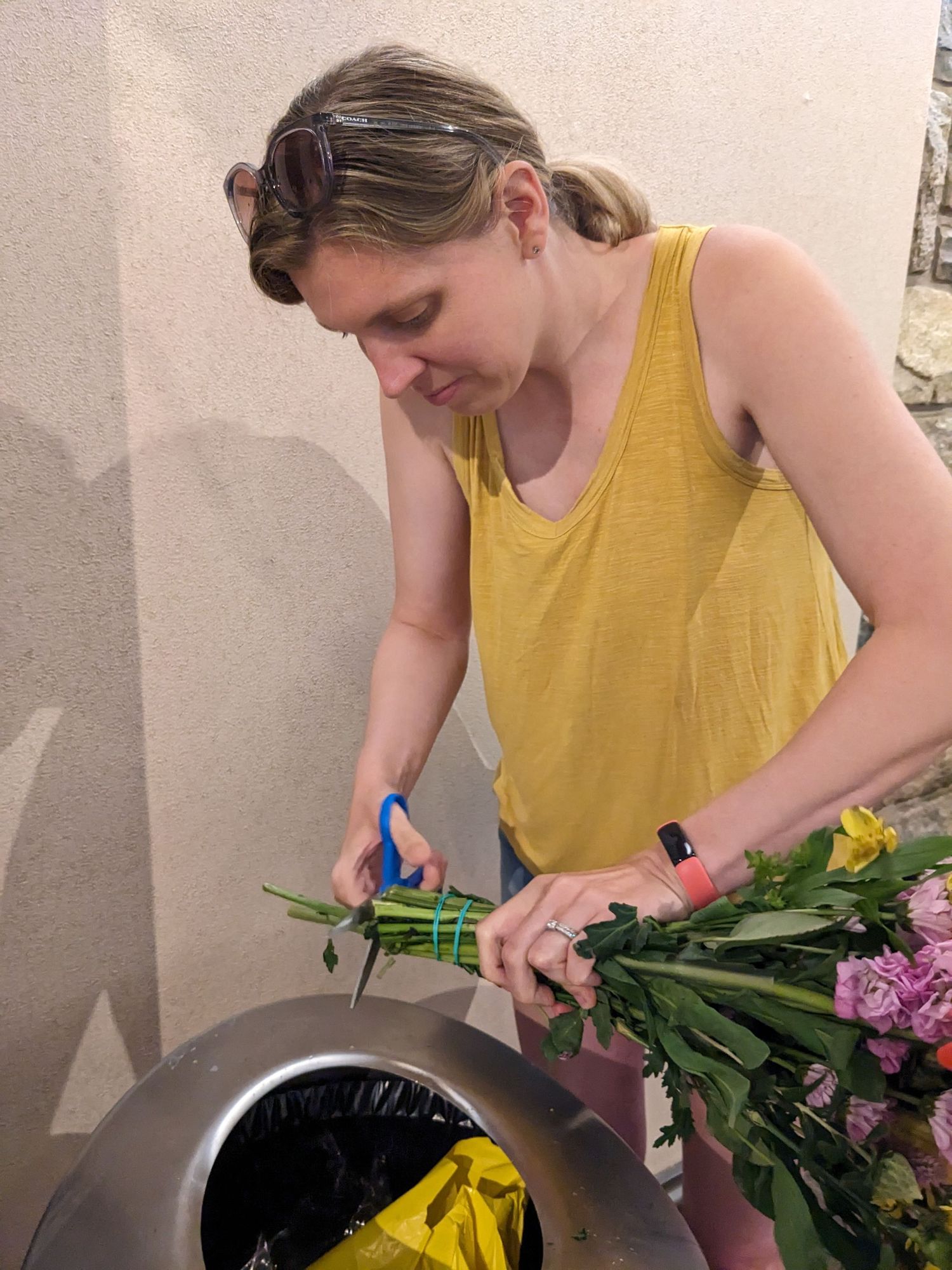 Person in yellow tank top trims flower stems over a container.