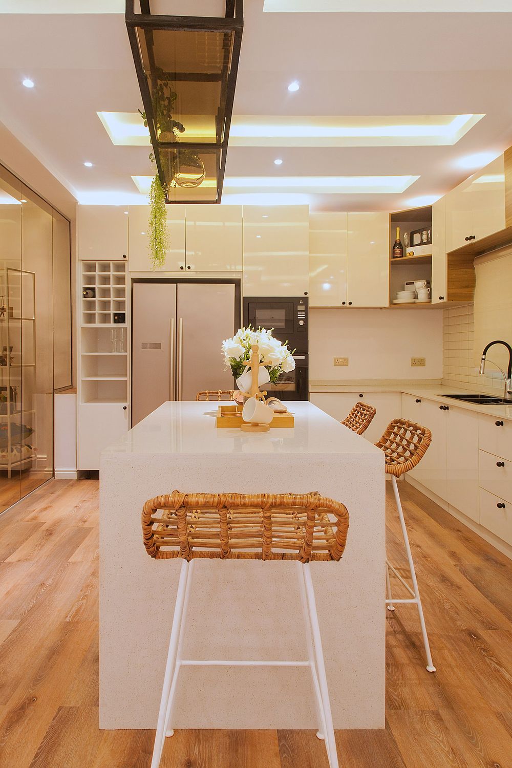 Contemporary kitchen featuring white cabinetry, wooden bar stools, and industrial-style overhead lighting.