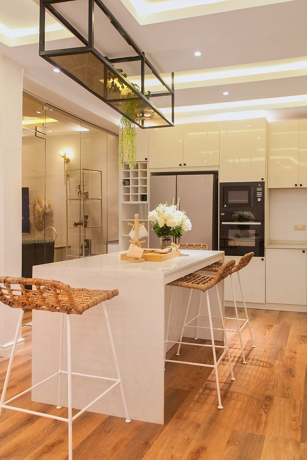 Sleek white kitchen with wooden floors, hanging plants, and modern industrial lighting fixtures.