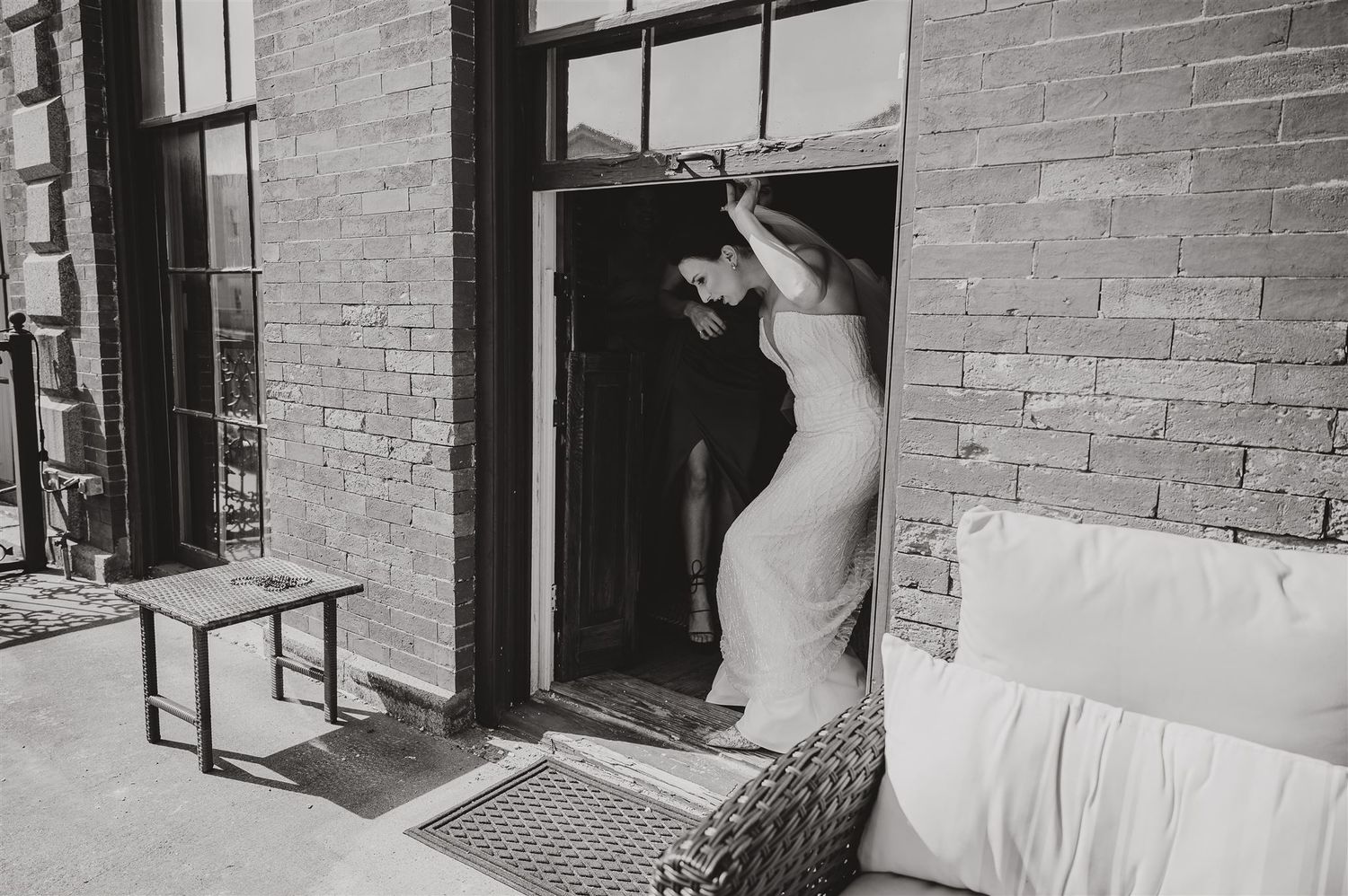 Black and white photo of person in white dress emerging from brick doorway.