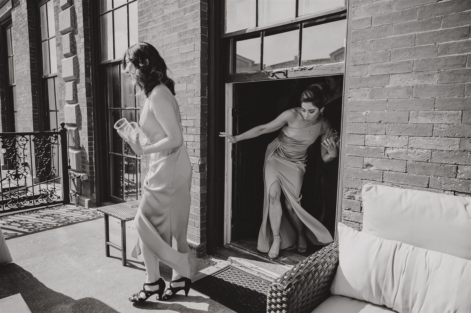 Black and white photo of two people emerging from doorway onto brick balcony.