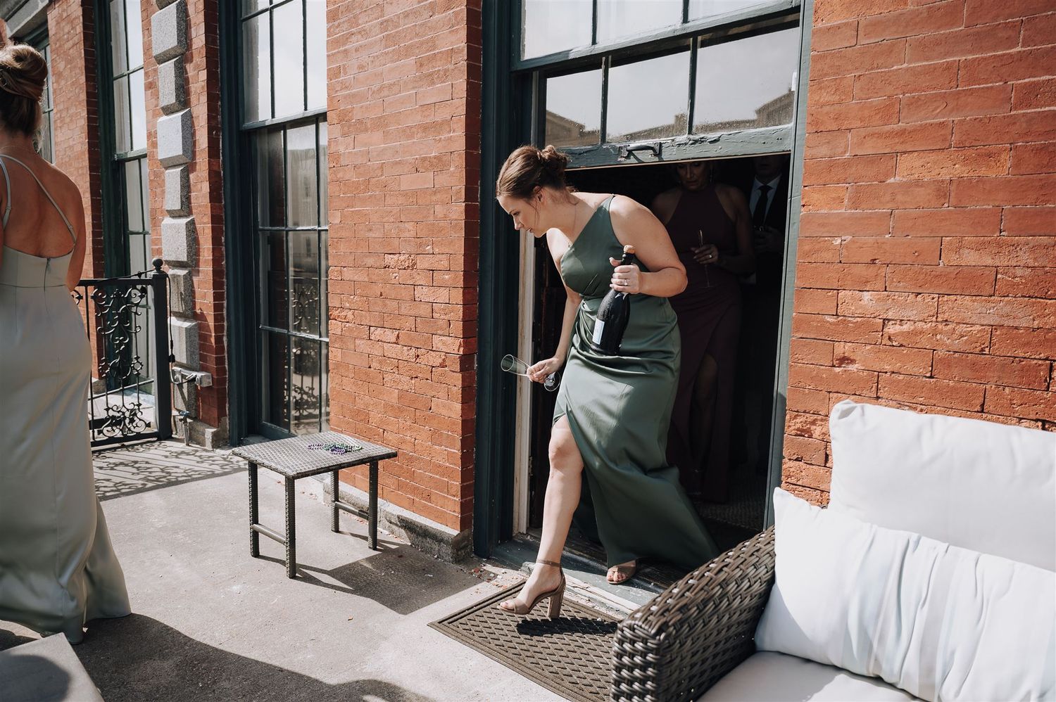 Person in sage green dress stepping through doorway onto outdoor terrace.
