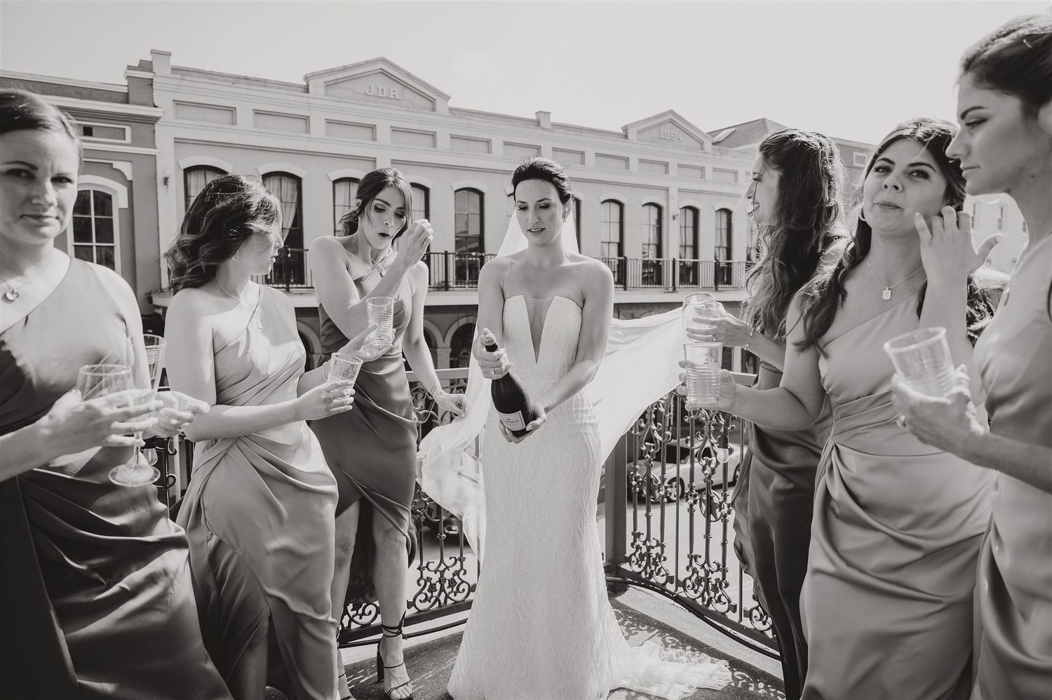 Black and white image of bridal party gathered on balcony with historic architecture.