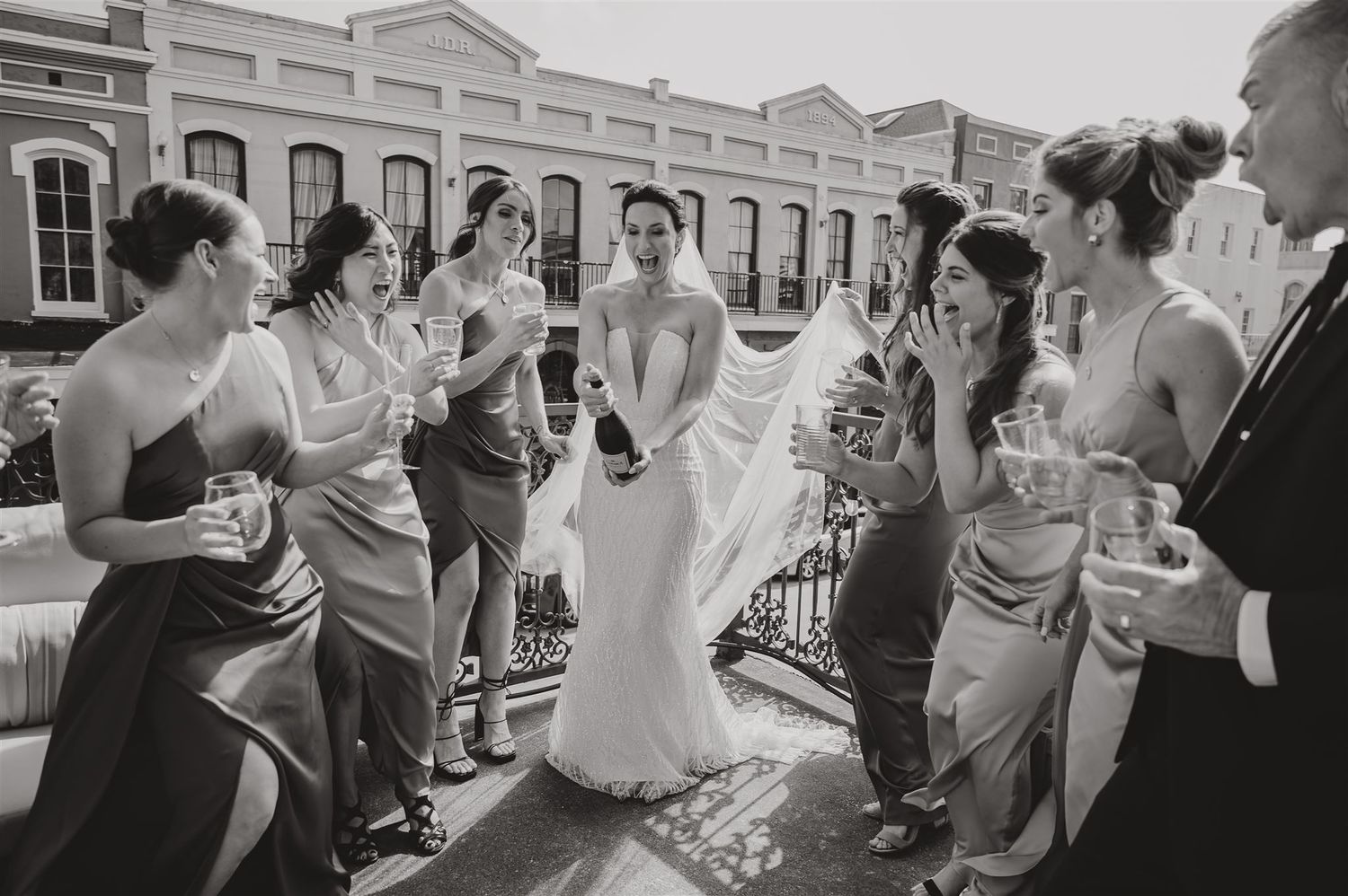 Black and white photo of wedding party celebrating on an outdoor balcony.