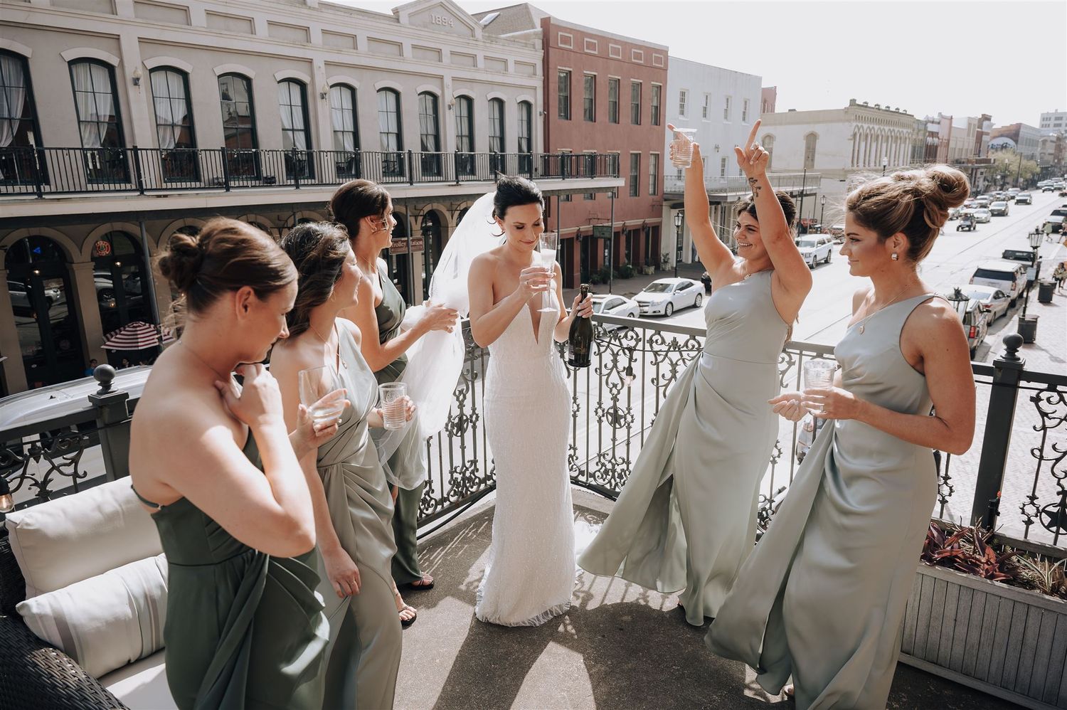 Bridal party in sage green dresses celebrating on vintage balcony in historic district.