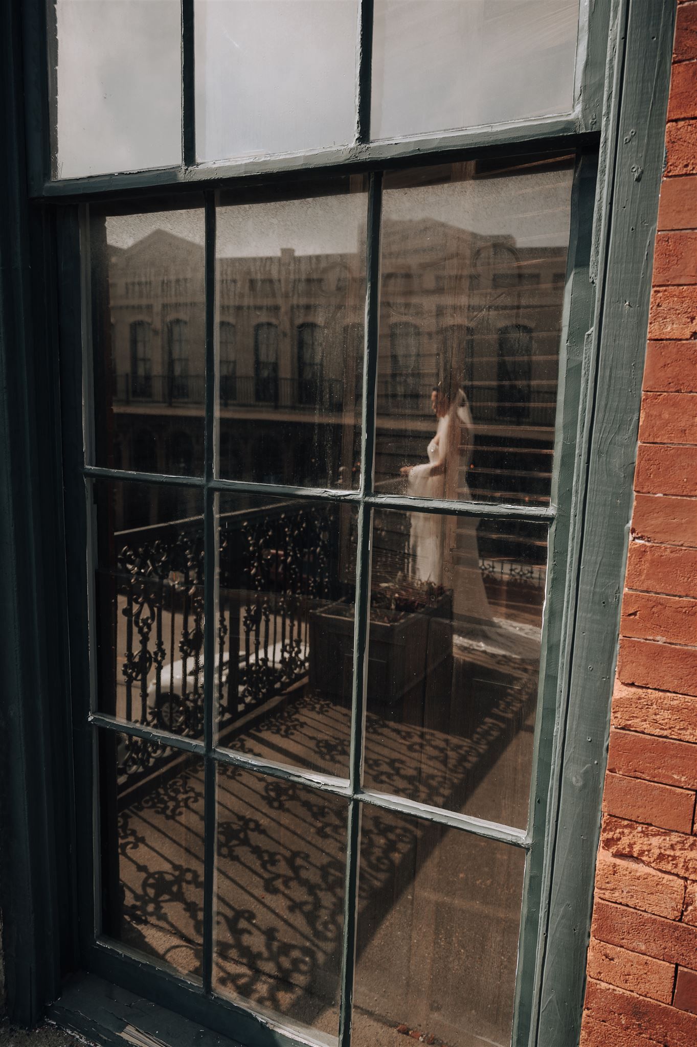 Antique window reflection showing ornate balcony railing and historic brick building facade.