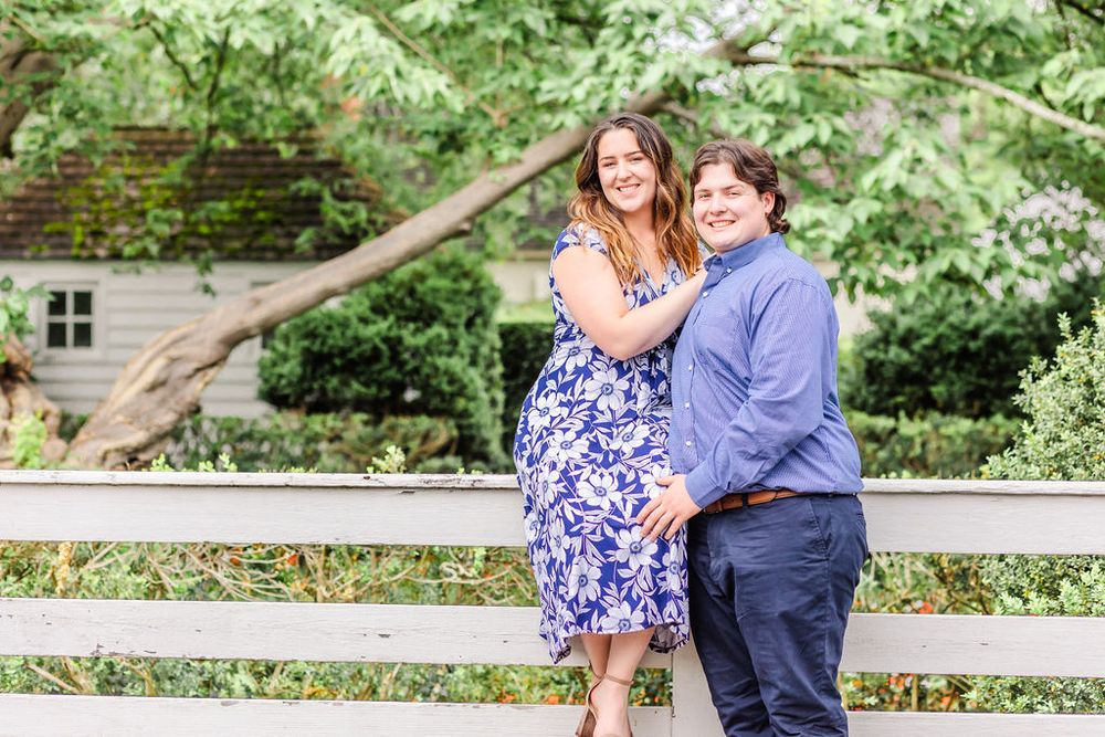 Romantic couple poses playfully on white bench in lush garden setting.
