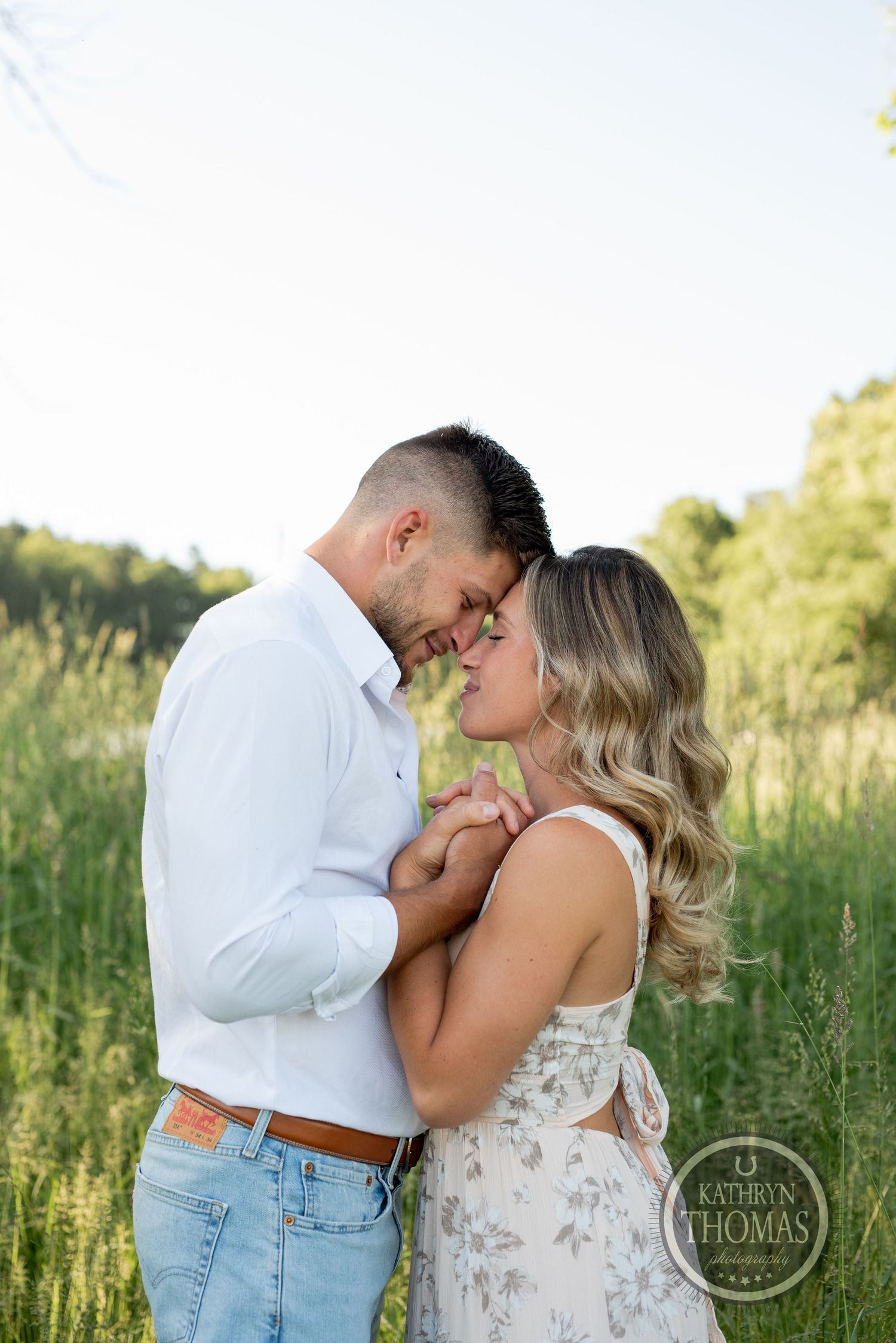 A tender moment between a couple in casual attire standing close in a sunny meadow.