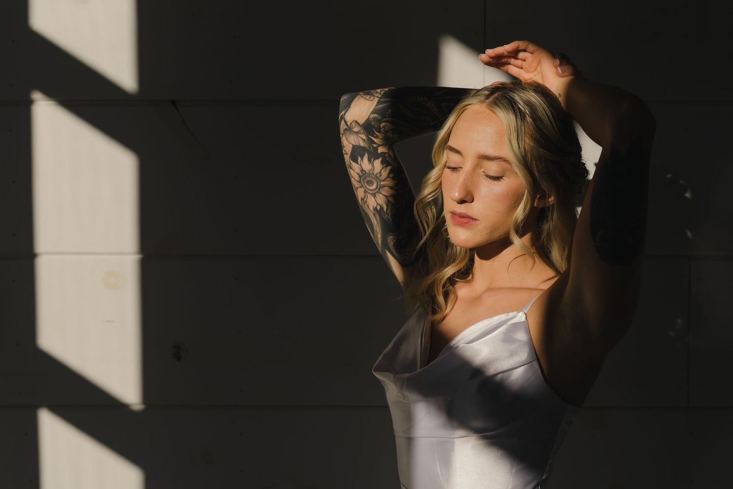 a bride in harsh window lighting posing with her arms resting on top of her head