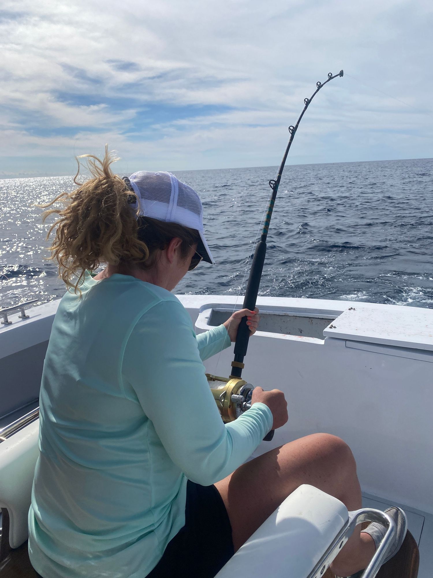 Deep sea fishing action on boat with rods and reels against blue ocean.