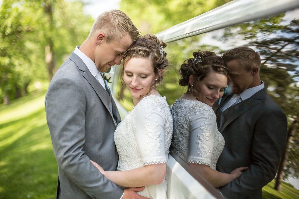 Bride and groom share a tender embrace outdoors, with a mirror reflection visible beside them on their wedding day.