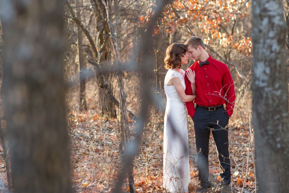 Couple sharing a romantic moment in an autumn forest, man in red shirt and woman in white dress surrounded by bare trees.