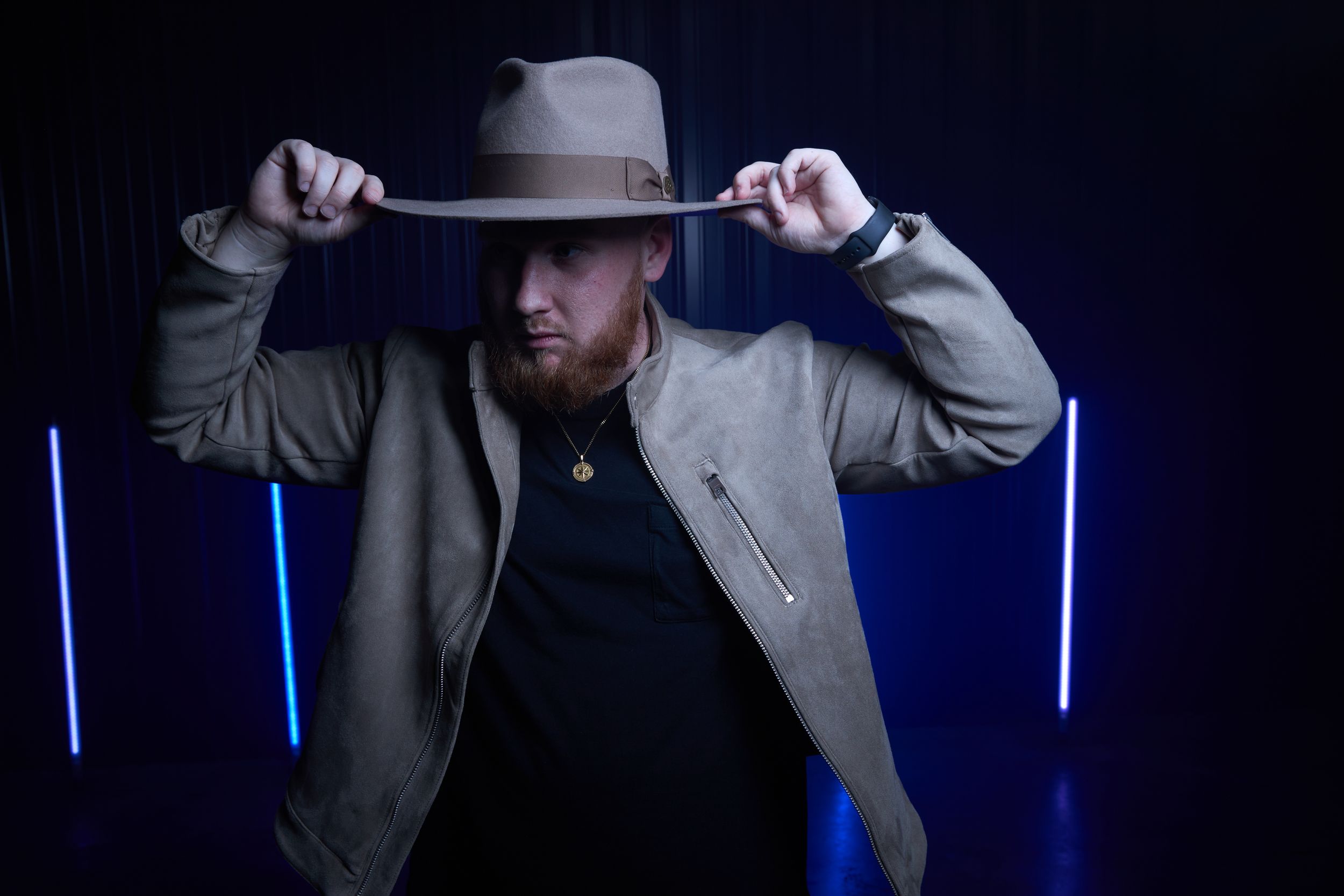 Dramatic portrait series in a dark studio with blue neon lighting and a brown hat creating moody atmosphere.