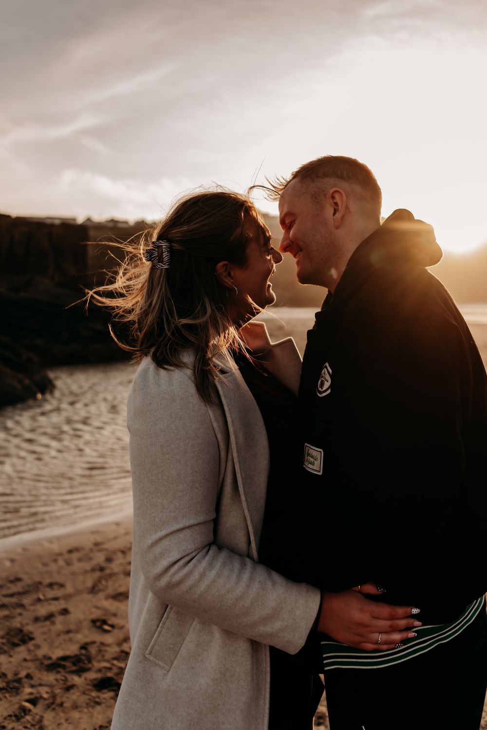 A couple shares tender moments at sunset on a beach as wind blows through their hair.