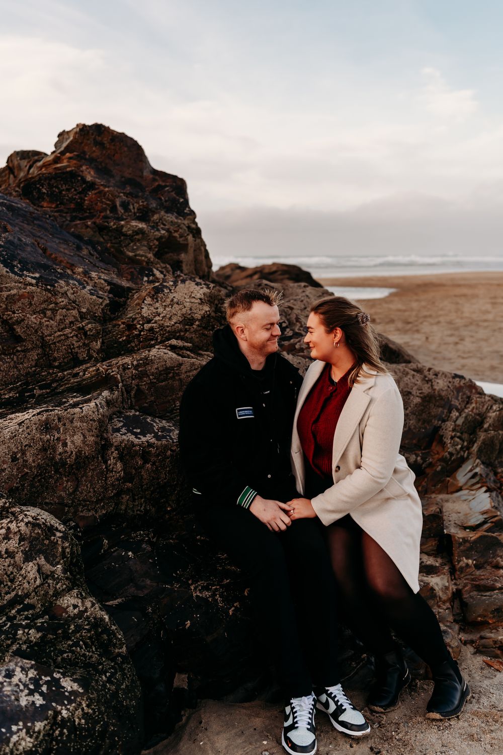 A couple sits intimately on coastal rocks at sunset sharing tender moments by the ocean.