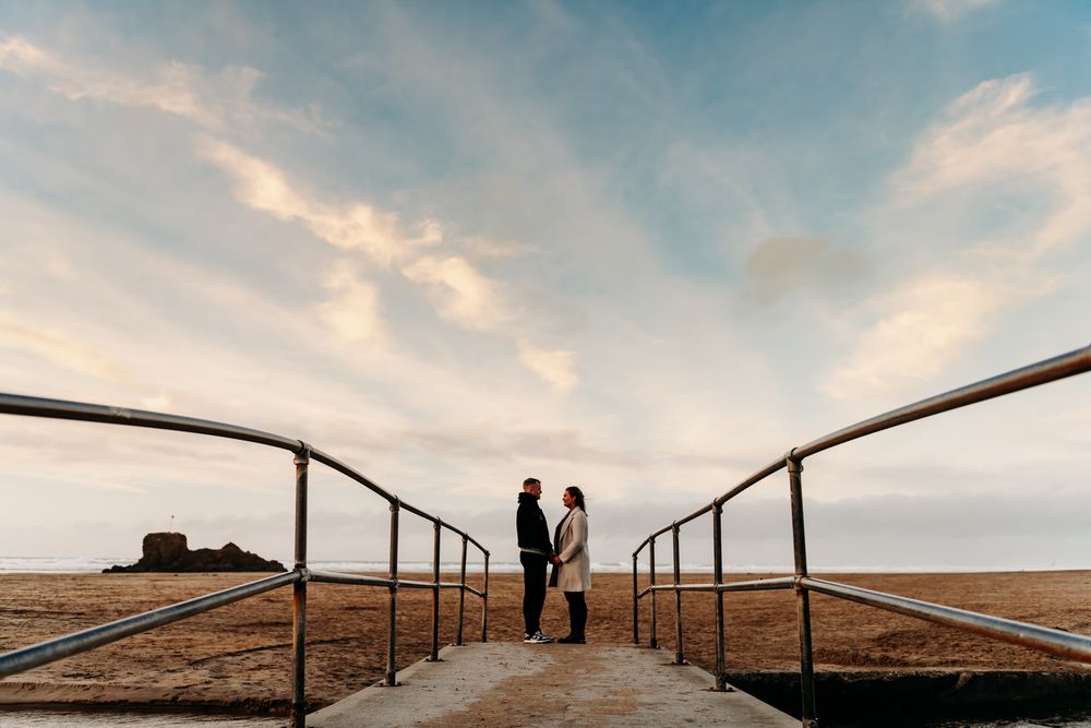 Silhouettes of people walking along a curved railing against a dramatic cloudy sky.