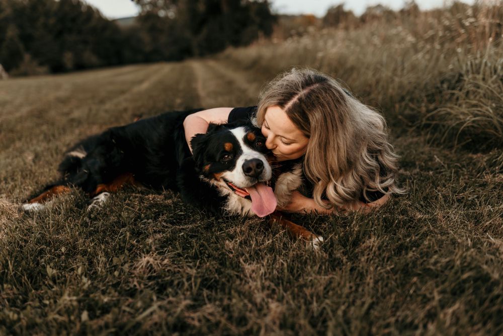A sweet moment between a dog and its companion lying together in the grass.