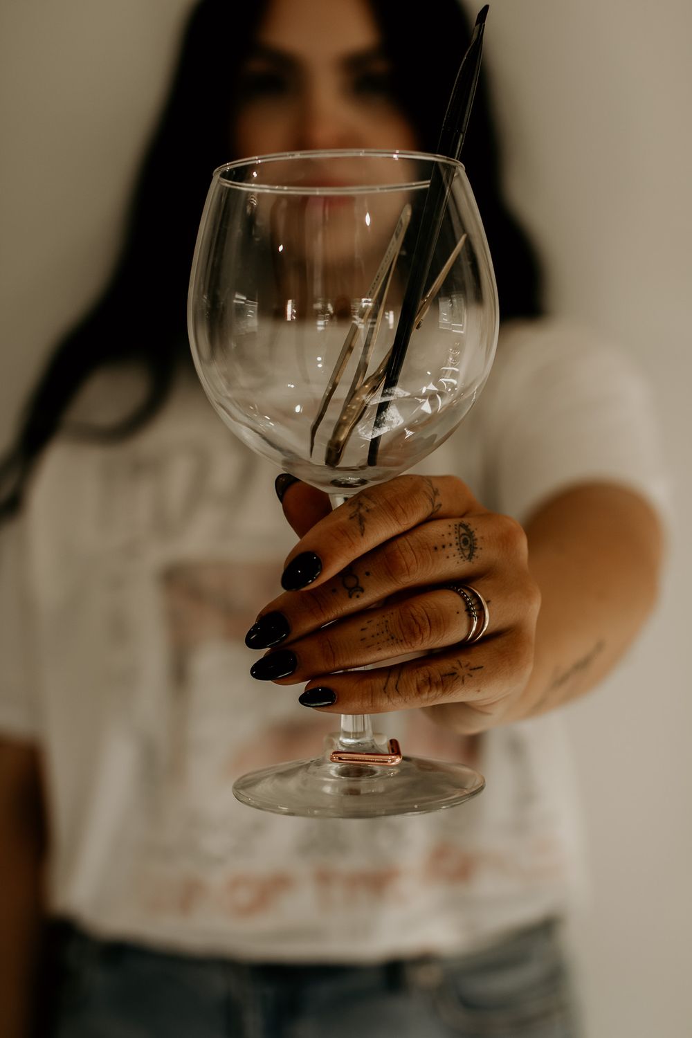 Hand holding large wine glass with dark manicure and minimal tattoos.
