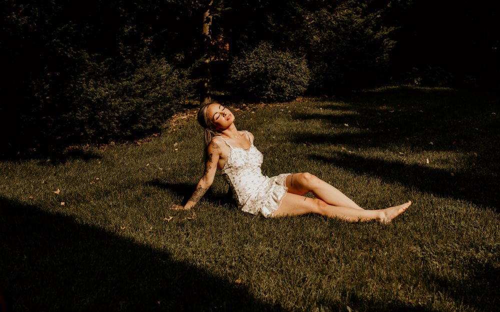 A dreamy summer portrait of a woman in white lace lounging on sunlit grass.