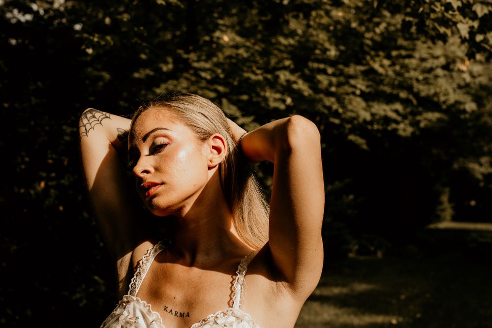 Artistic portrait of a woman basking in warm sunlight against a dark garden background.