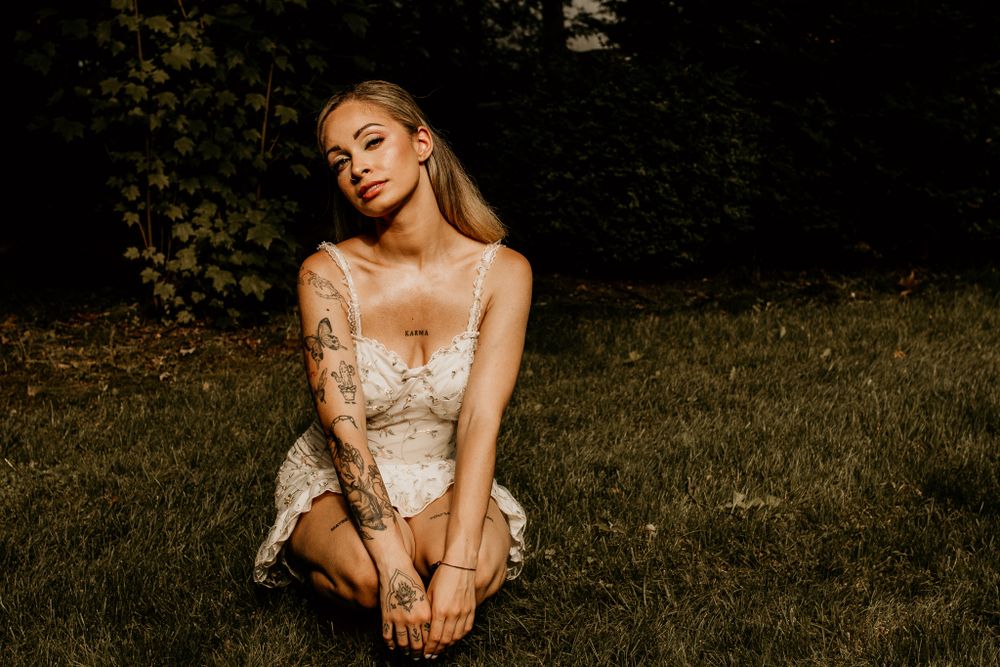 A woman in a delicate lace dress poses in golden sunlight on a grassy lawn.