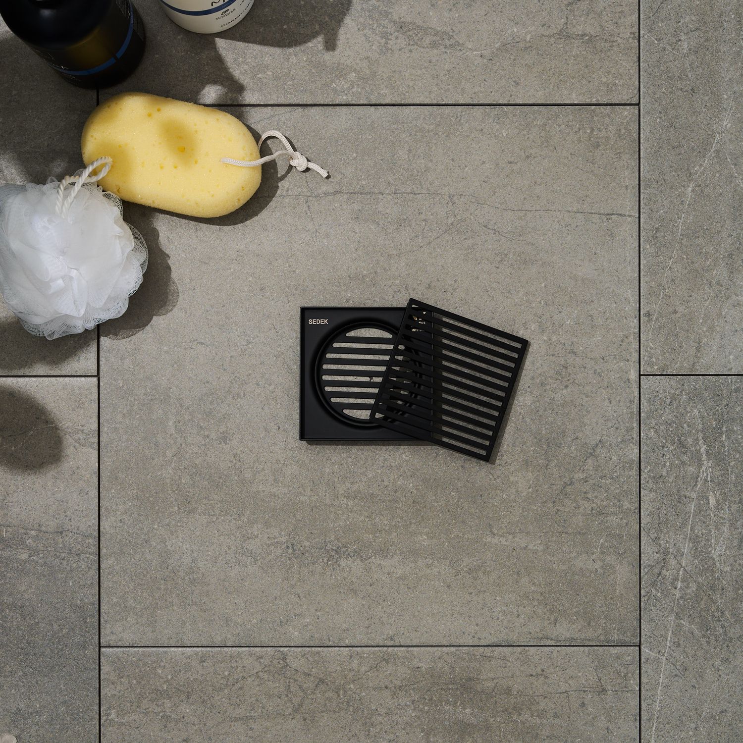 Black square grates sitting on tiles with bath sponge, luffa, and shampoo