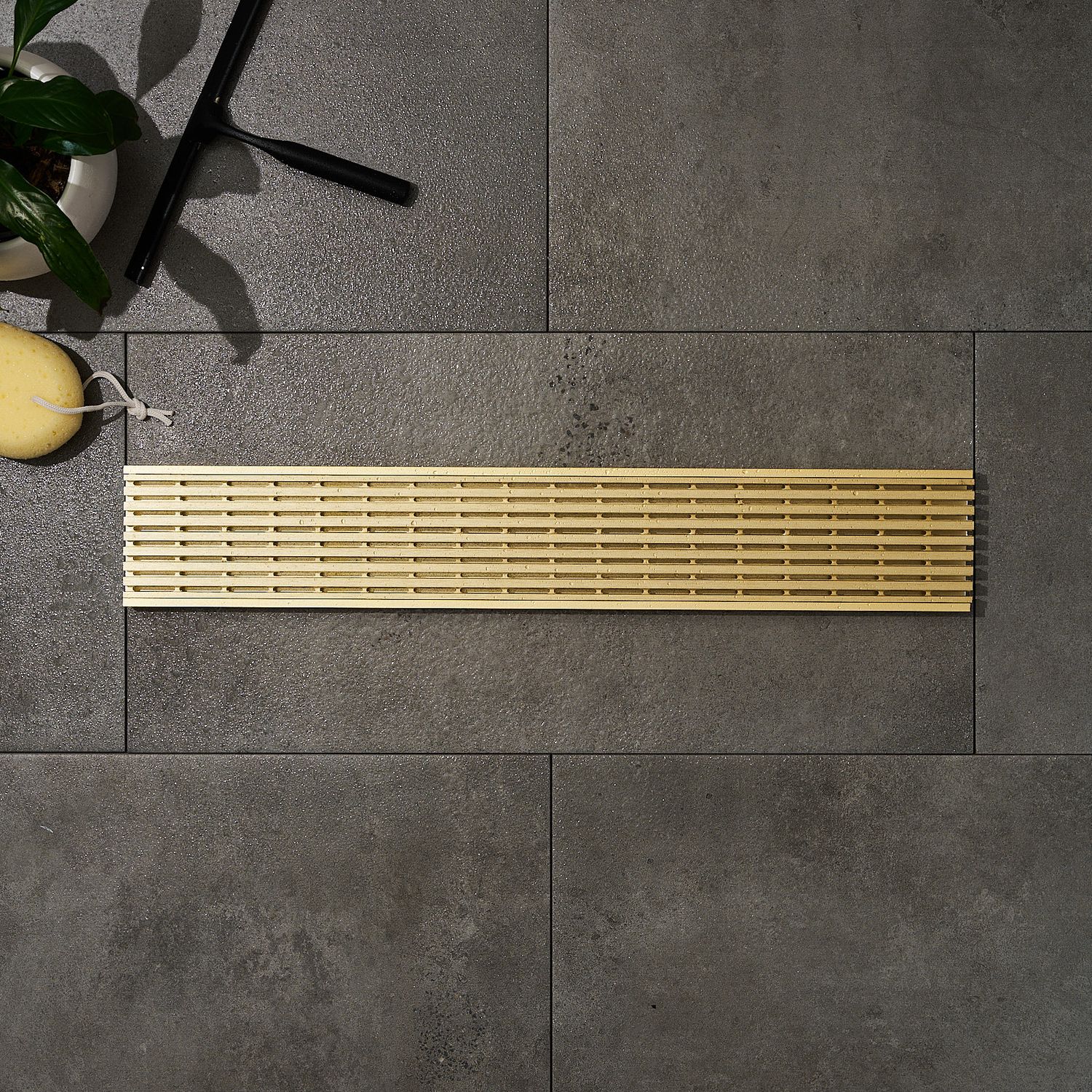Gold rectangular grates grates sitting on tiles with bath sponge and green plants