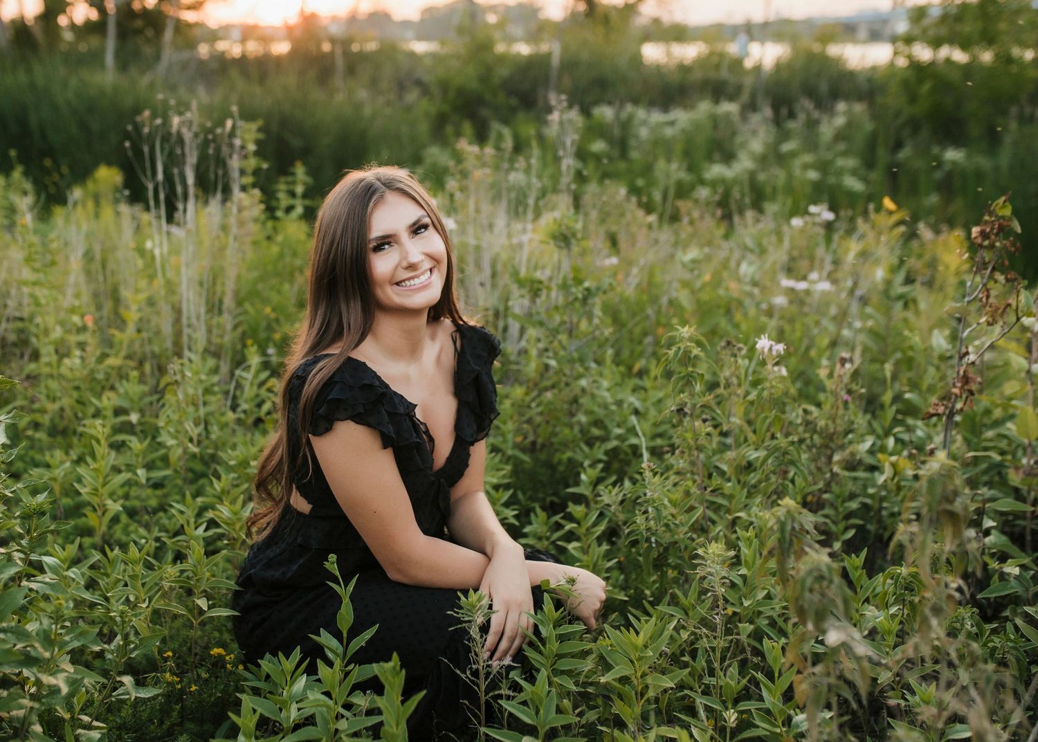 Woman in black dress poses in wildflower field at sunset.