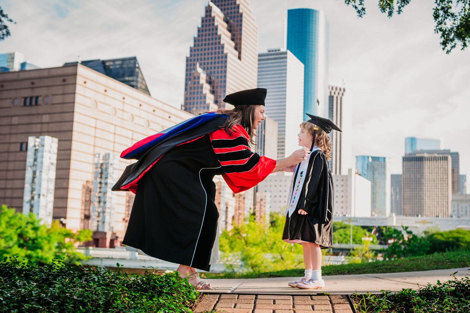 Graduate students in caps and gowns celebrate their commencement ceremony on a sunny day with city buildings in the background.