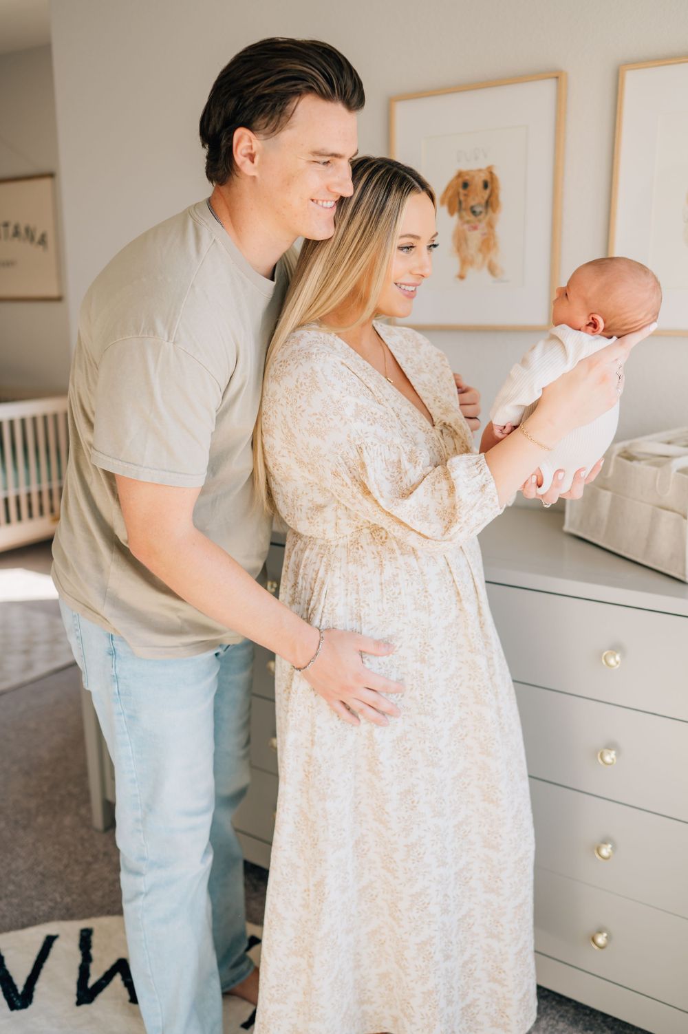 Family shares tender moment near white dresser in nursery with framed artwork.