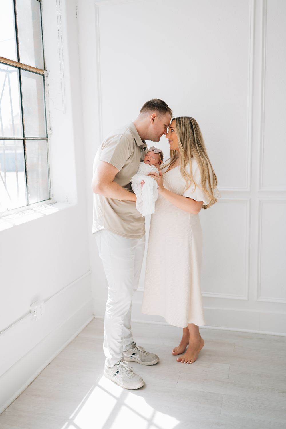 Intimate family moment in a bright white minimalist room with natural window light.