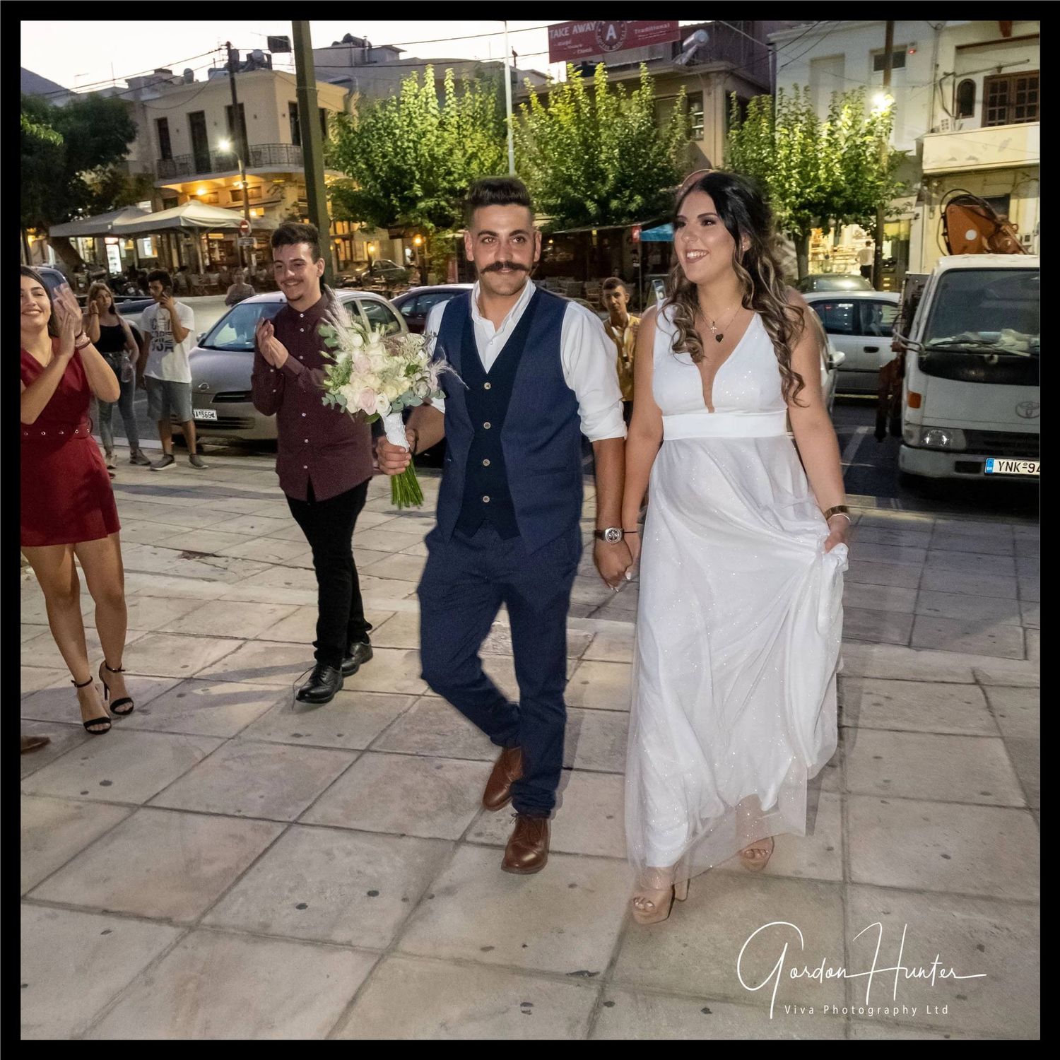 Greek Bride and Groom walking to the park. Groom holding Bride's bouquet.