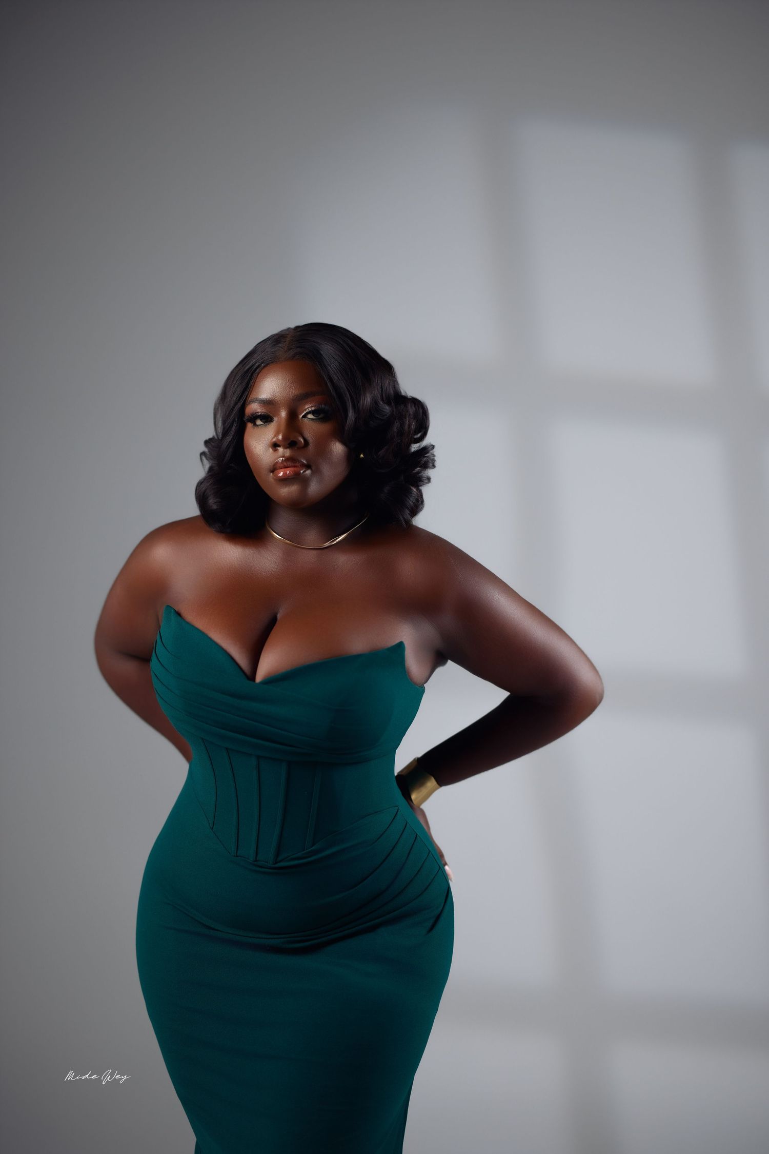 A figure in an emerald green dress poses elegantly against a light gray studio backdrop in a series of artistic portraits.