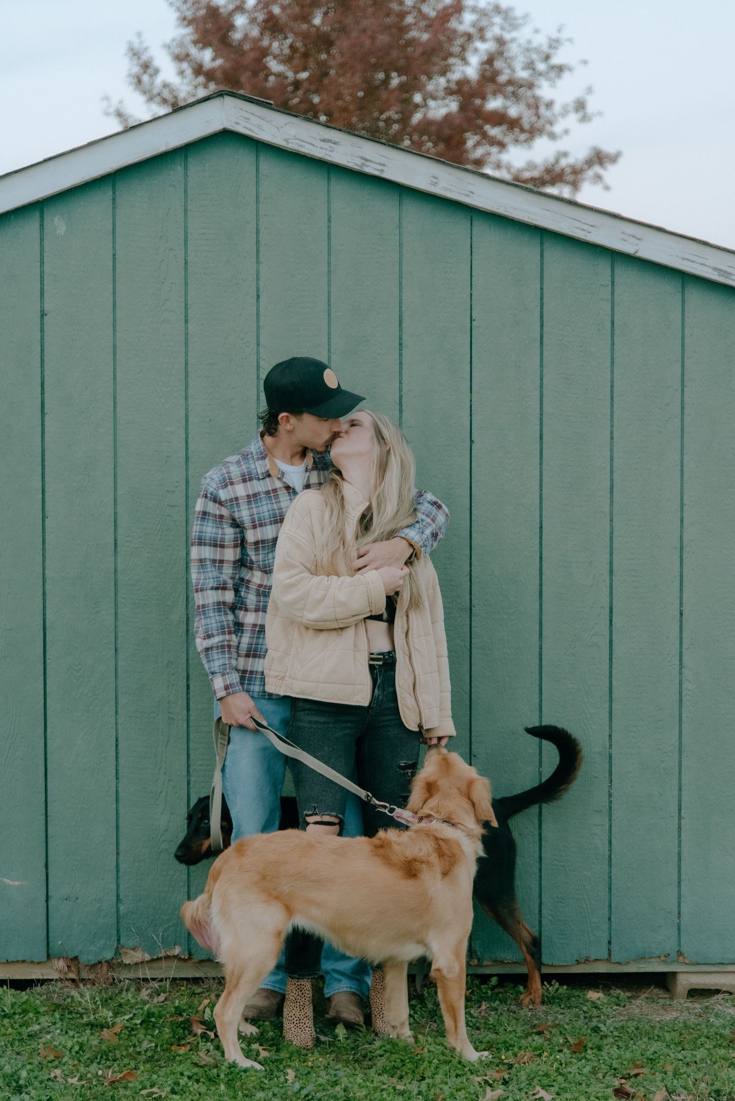 Couple posing with their golden retriever dog against a mint green shed wall.