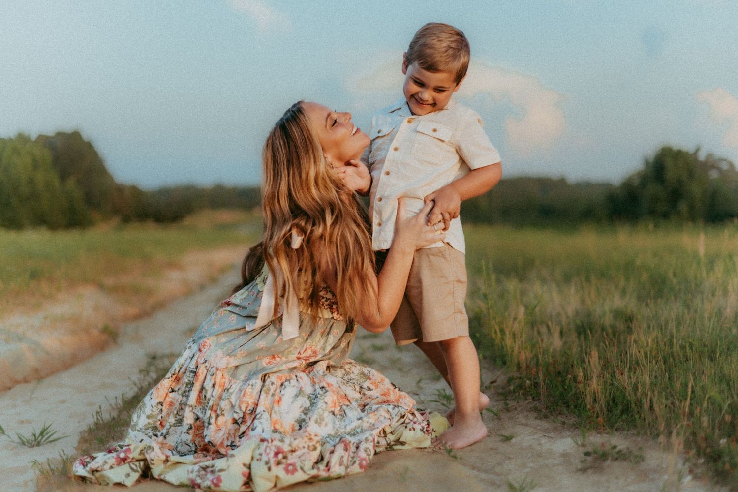 Candid outdoor moment between parent and child in summer meadow at sunset.