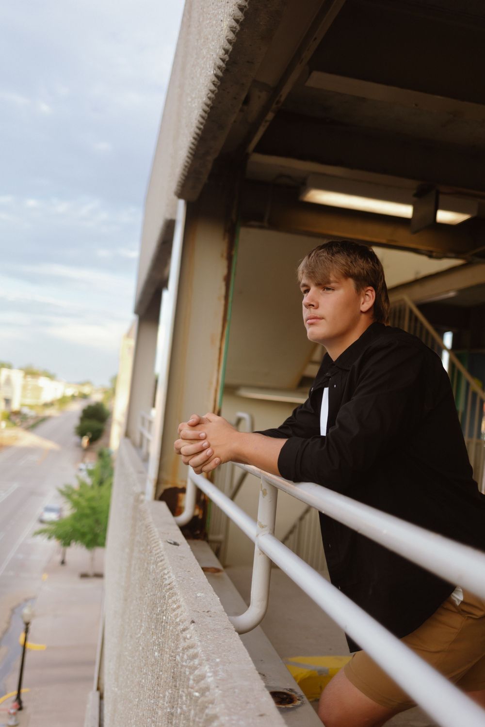 Someone leans against a white railing on a covered walkway at dusk while looking into the distance.