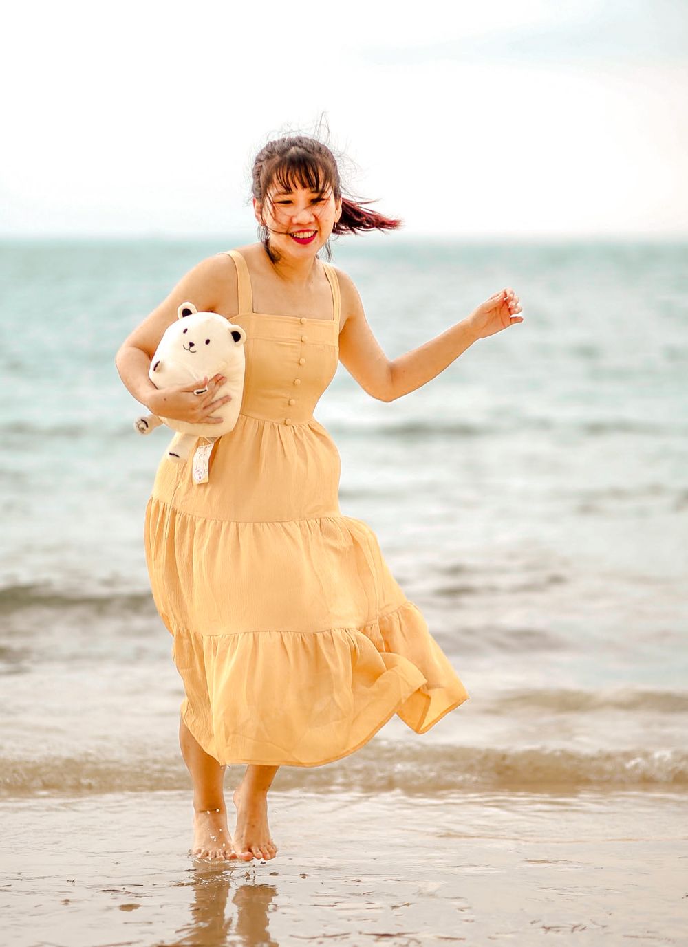 Woman in a flowy dress twirling in an open space, running freely at the beach with sunlight streaming through in Singapore photoshoot