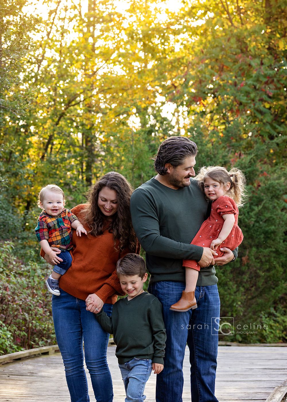 A family shares candid moments together while walking on a path surrounded by autumn trees at sunset.