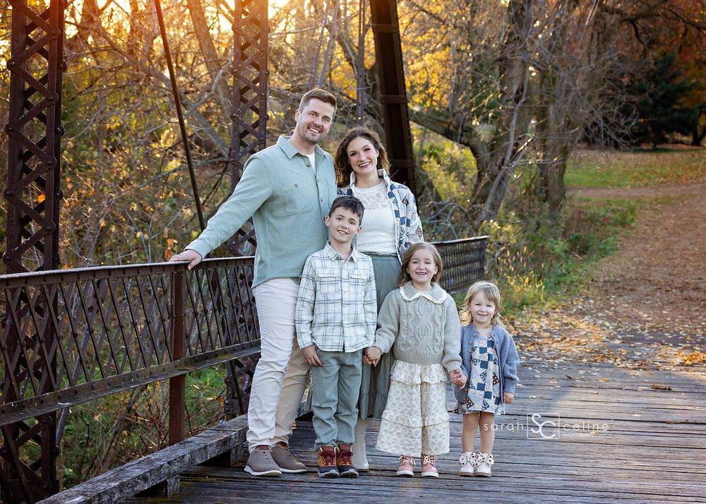 Family of five posing on wooden bridge during autumn sunset.