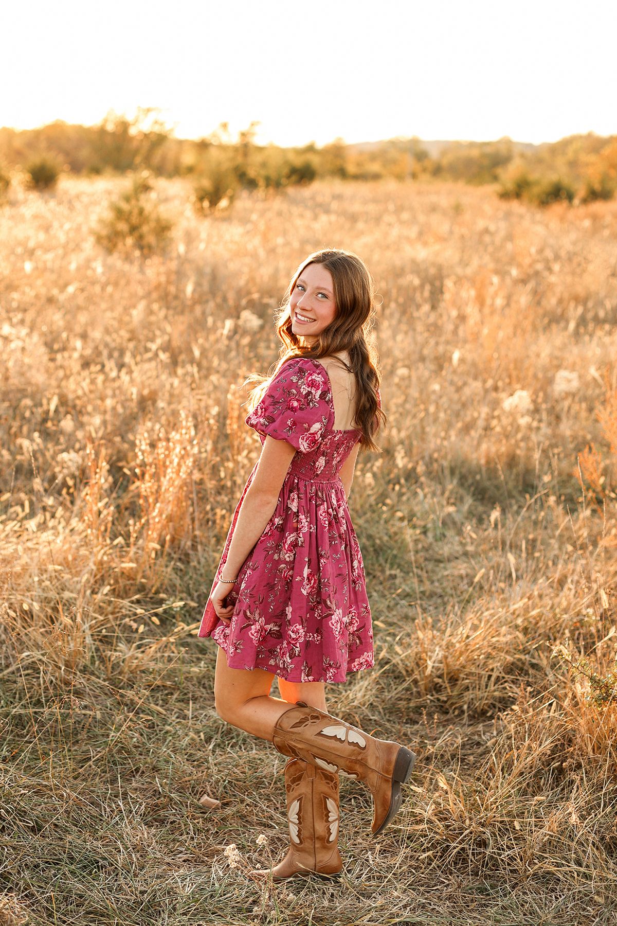 Senior girl in high school, pink dress and cowboy boots standing in field smiling at the camera, Keli Tetzlaff Photography