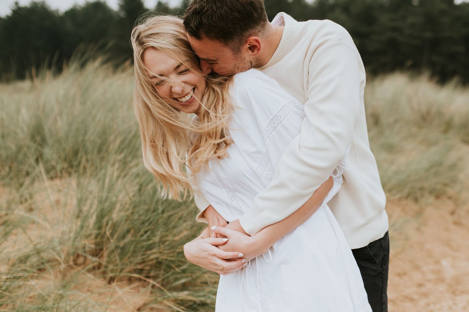 Romantic couple shares tender moments in a field of tall grass during golden hour sunset photo session in Norfolk