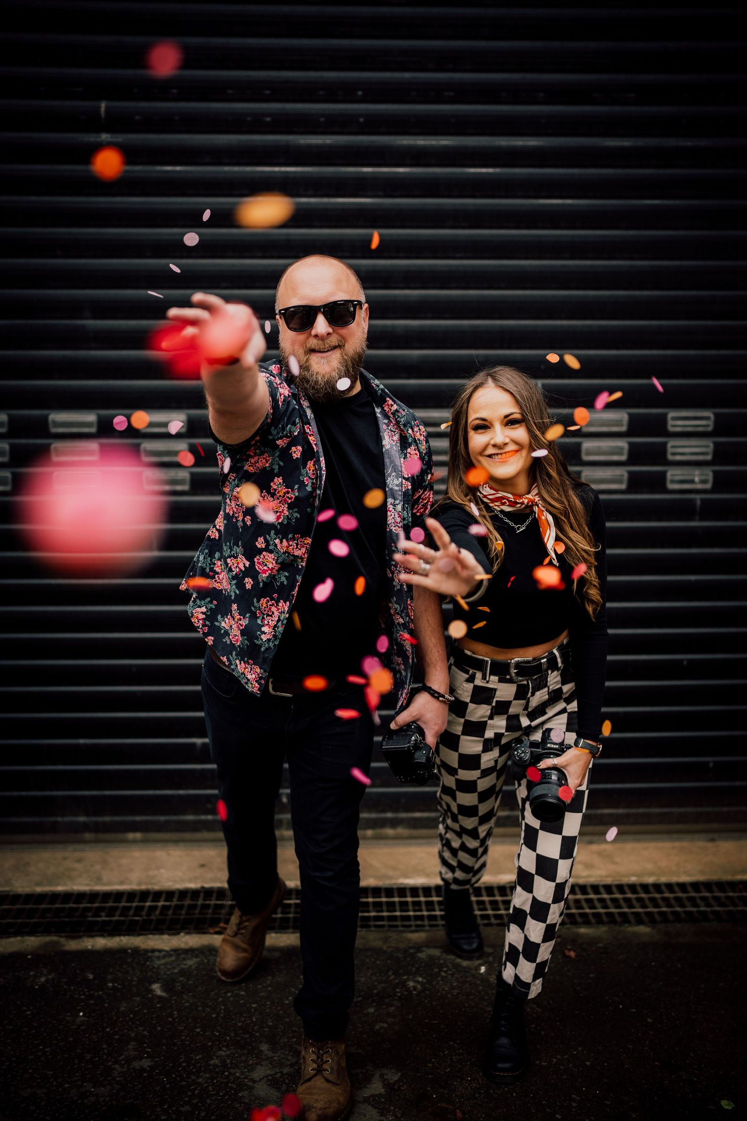 Couple throws colorful confetti against black wall in artistic wedding photo. Worcestershire Wedding photographer.