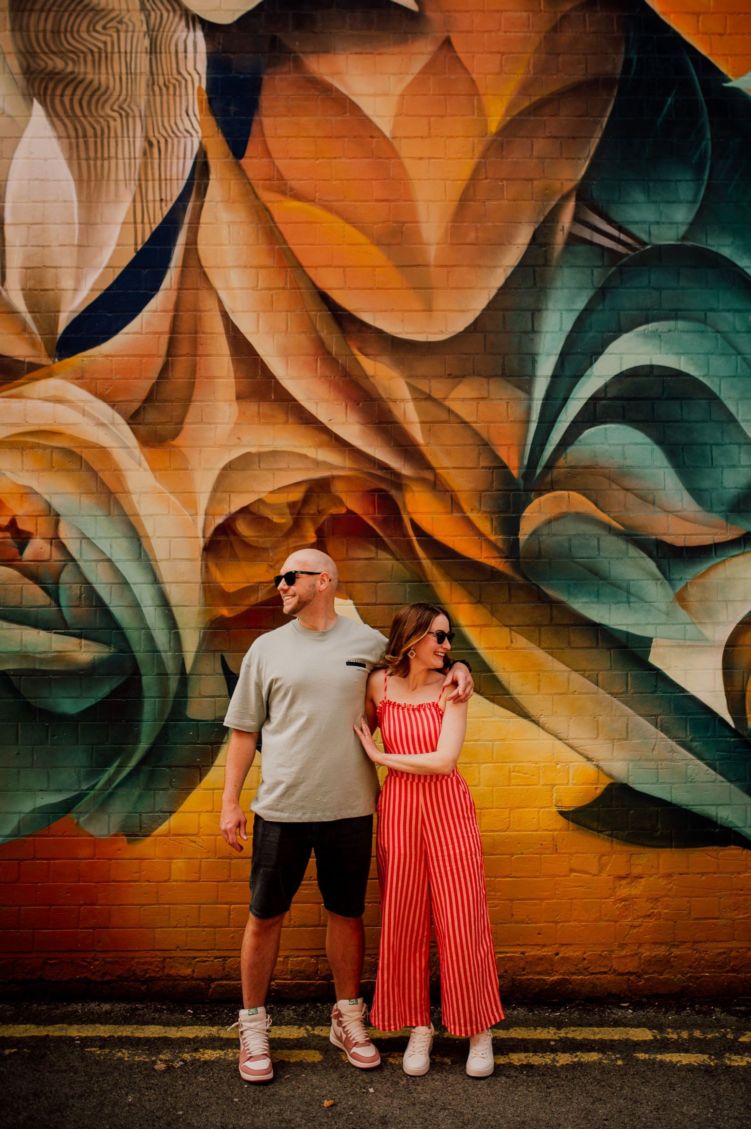 Couple standing against vibrant mural of large pink flowers on dark blue wall. Worcestershire Wedding photographer.