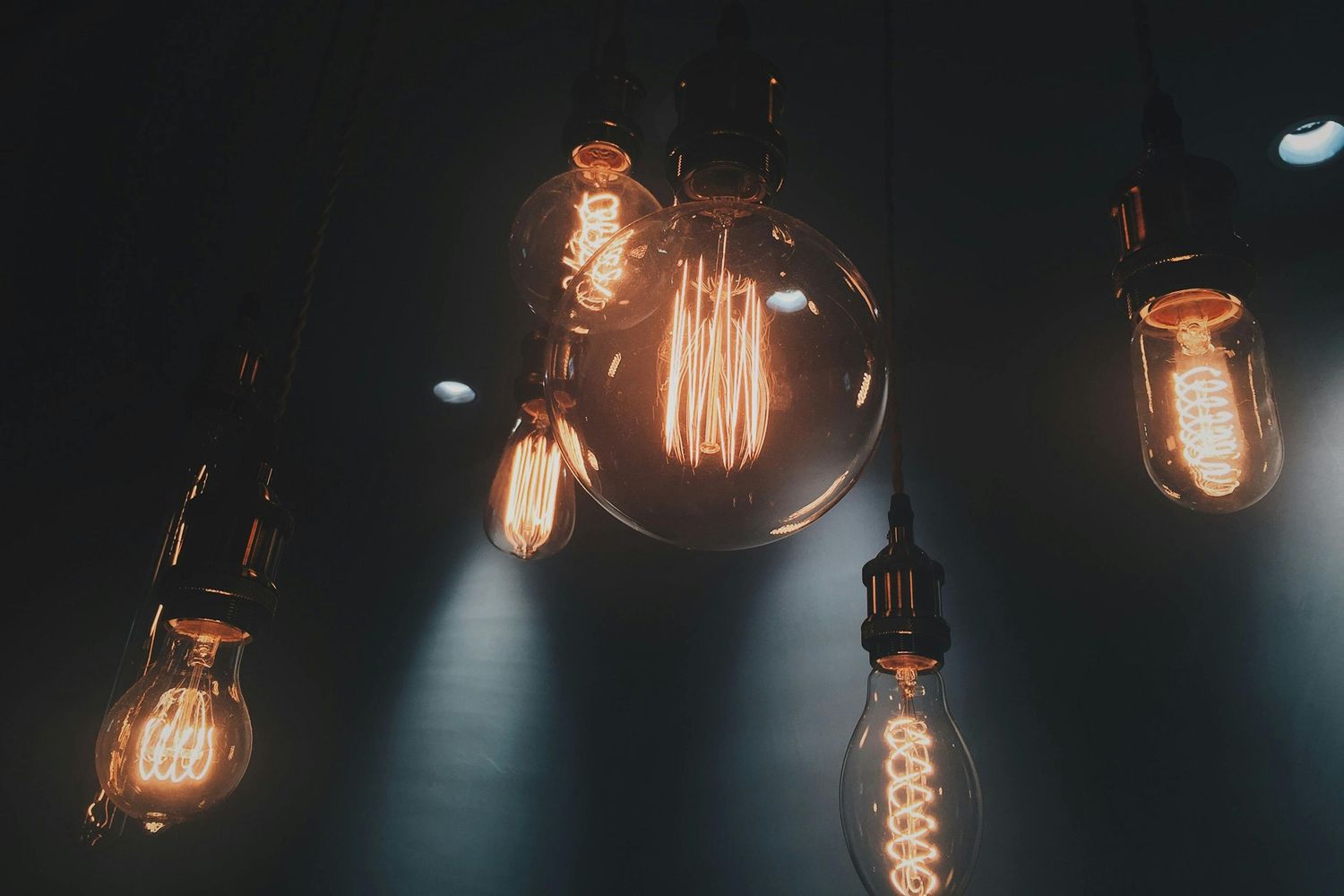 Several vintage-style Edison bulbs with warm glowing filaments hang from above against a dark background.