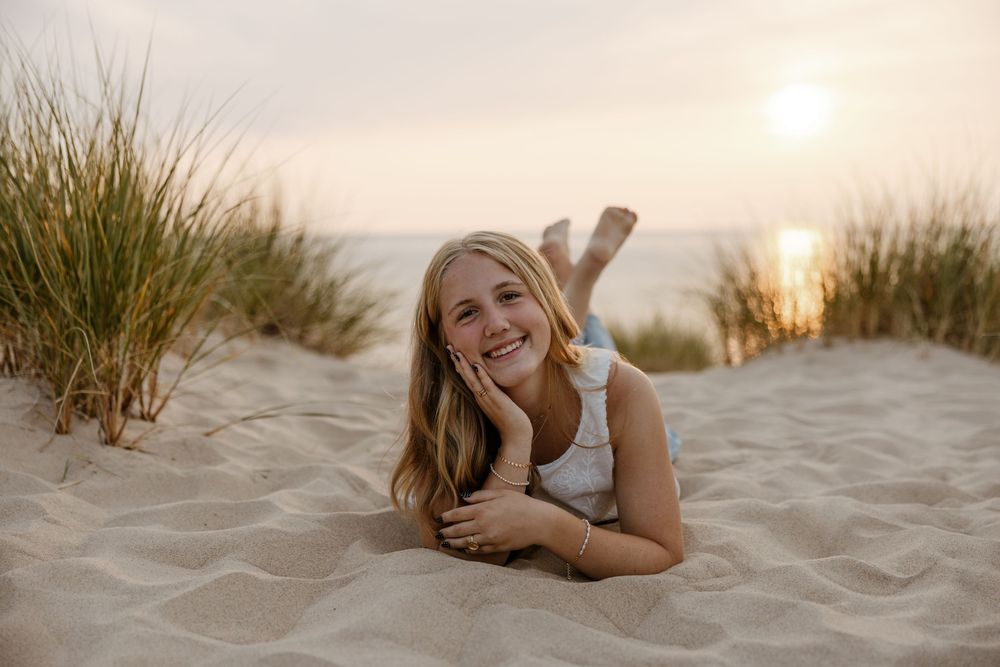 A young woman relaxing on the beach at sunset, lying in the sand and smiling. Fort Worth Texas senior photographer.