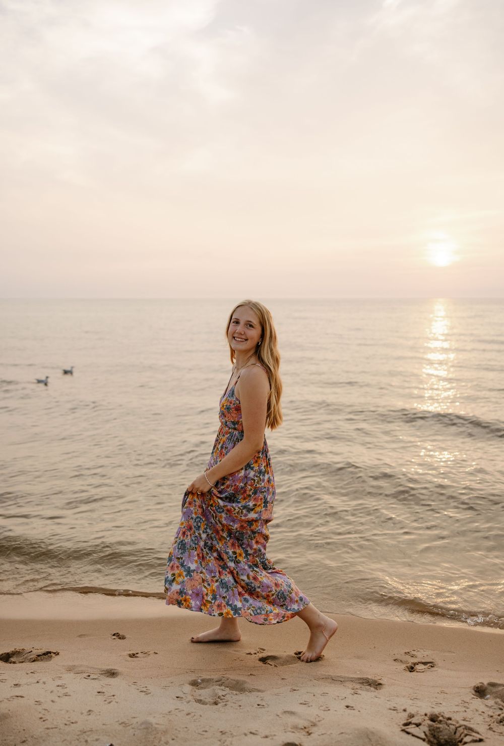 A woman in a colorful floral dress walks along the beach at sunset, with the ocean and sky in the background. Fort Worth Texas photographer.
