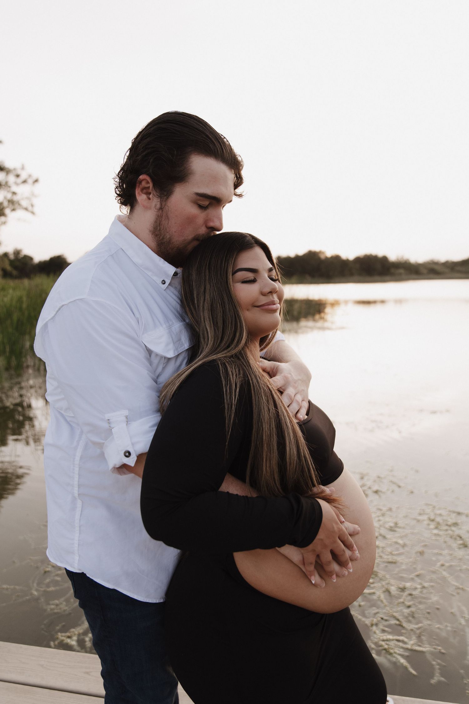 A maternity photo of a couple sitting in a rustic field at golden hour.